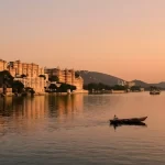 Udaipur Tour with Boat Ride & City Palace Entry showing a boat on Lake Pichola during sunset with the City Palace on the lakeside.